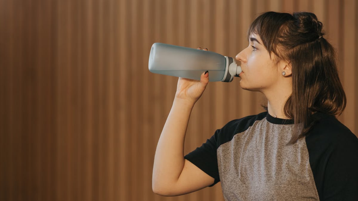 Side view of a woman drinking water from a bottle, promoting healthy lifestyle and fitness.